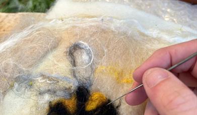 A hand holding a needle threading felt to create a bee pattern