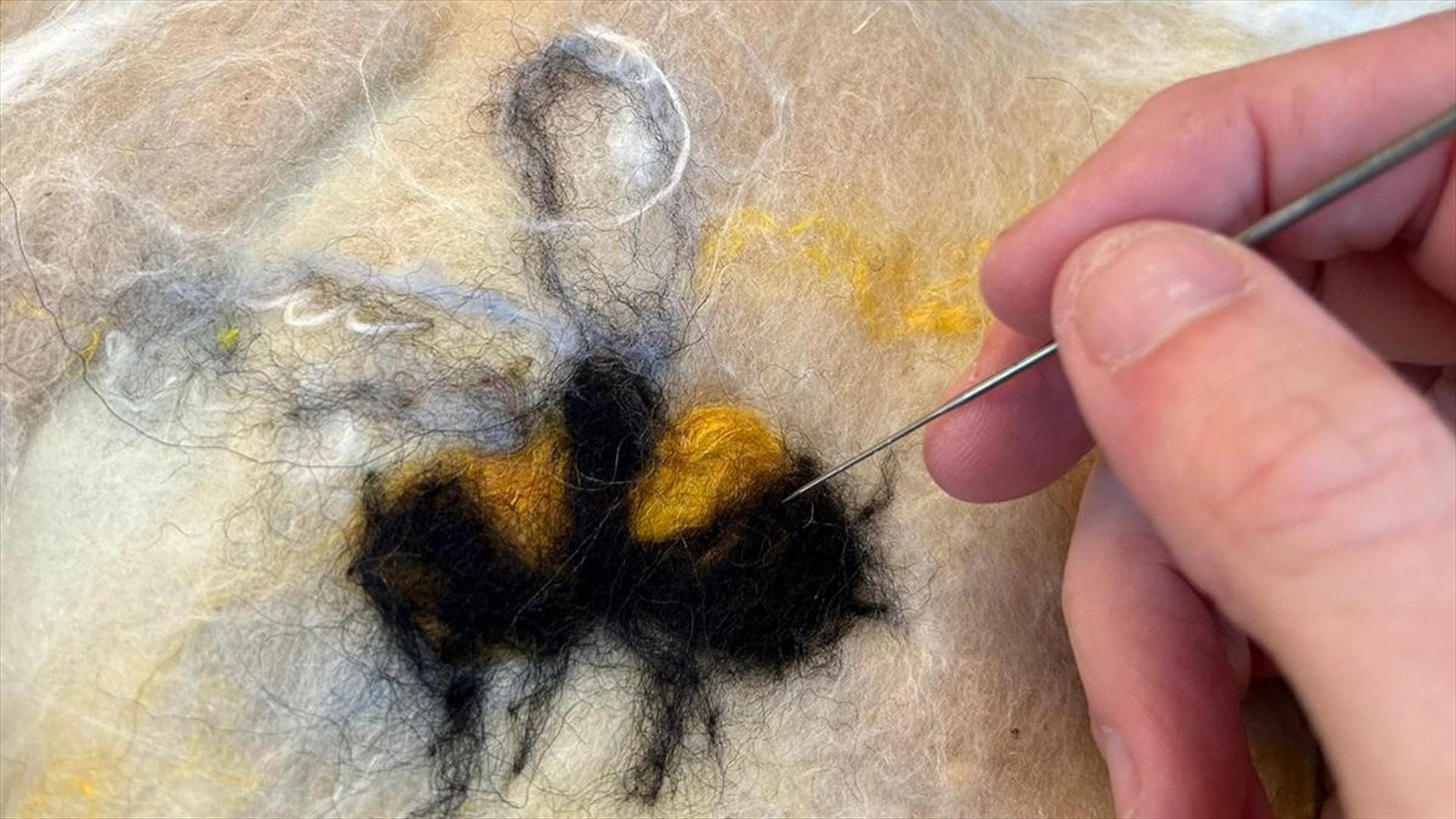 A hand holding a needle threading felt to create a bee pattern