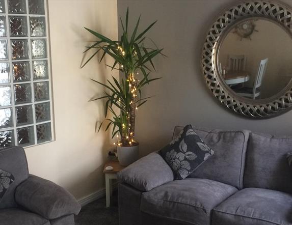 a photo showing a living room with sofas, a mirror, a plant and a window