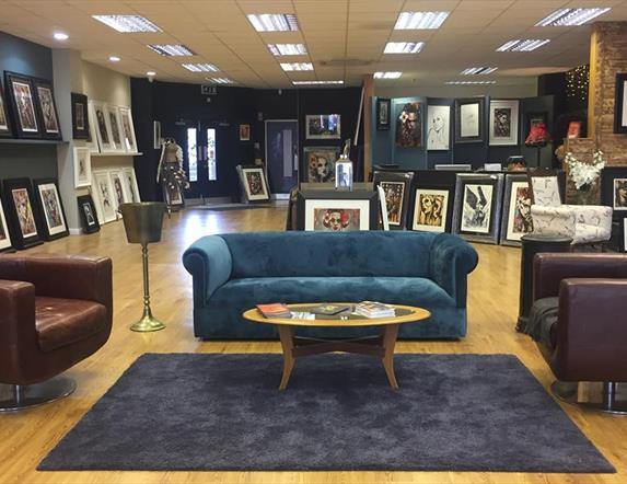 Photo of the inside of the gallery showing seating area and paintings on display for sale