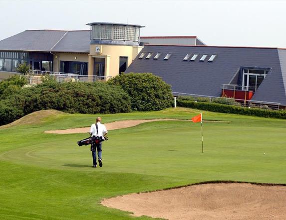 Photo of Club house and a golfer on the green to the forefront