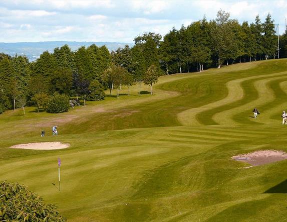 Golfers on the green with woodland and coast in background