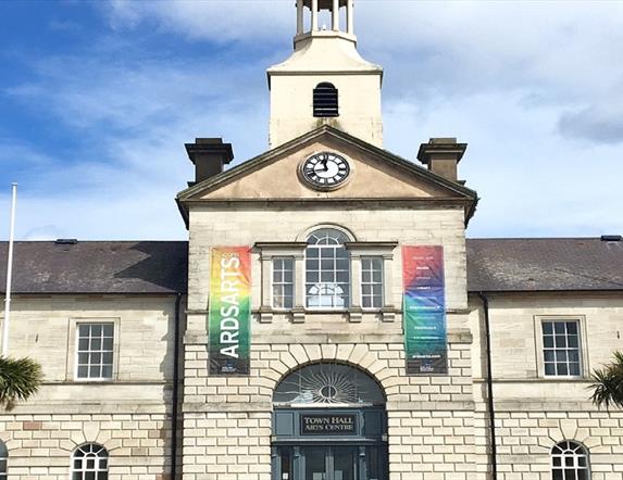Photograph of the front exterior building of Ards Arts Centre previously the Town Hall, with backdrop of blue sky and two banners flanking the front w