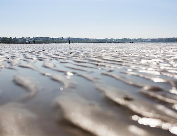 Close up photo of the ripples of sand on Ballyholme Beach with the promenade and bathers in backdrop