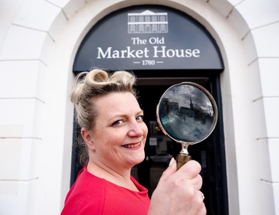 Miss Scarlett holds a magnifying glass at the doorway of The Old Market House, Bangor
