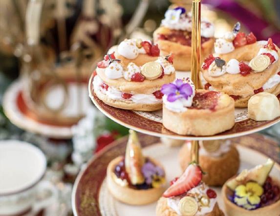 Elegant three-tiered cake stand filled with artisanal pastries, fruit tarts, and floral-decorated sweets, set against a softly blurred background with