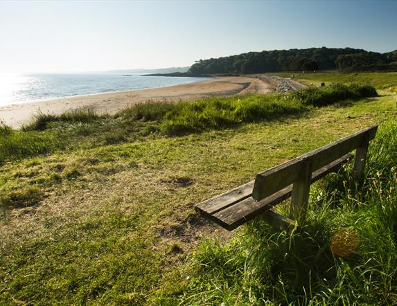 An image of Helen's Bay beach from the shore with a bench ready to welcome someone to sit