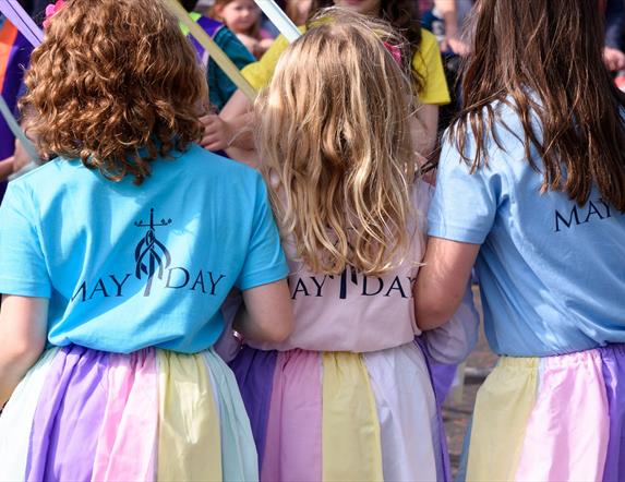 A photo of a trio of little girls taking part in the annual maypole dancing dressed in pastel skirts to match the ribbons of the Maypole