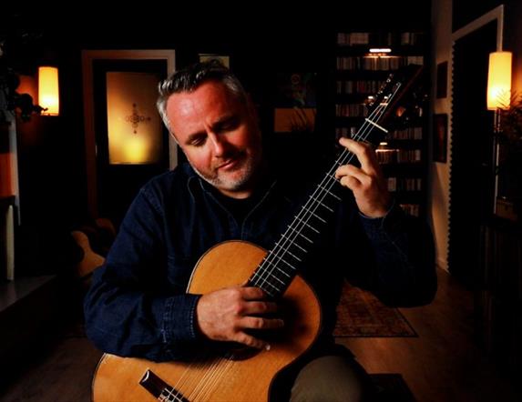 Guitarist Matthew McAllister playing guitar in a small dark room with some mood lighting.