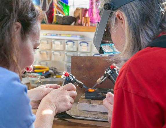 Two ladies with small torches melting down some gold in contemporary studio