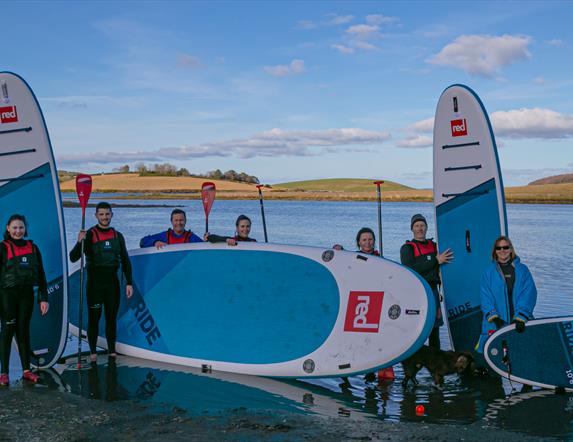 Paddleboarders of all ages standing with boards and paddles back from a session on the waters of Ballymoran Bay