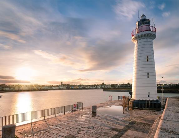 image of lighthouse and pier with sunset over the water in the background.