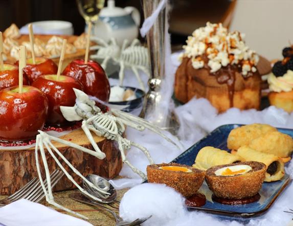 Table set up with food including toffee apples, scotch eggs, sausage rolls, cake and cupcakes with halloween decor