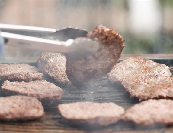 hand turning a burger on the bbq with a blue glove on it