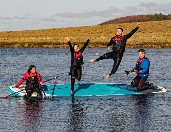 Four paddleboarders sharing a board, two of them jumping into the water
