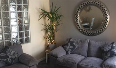a photo showing a living room with sofas, a mirror, a plant and a window