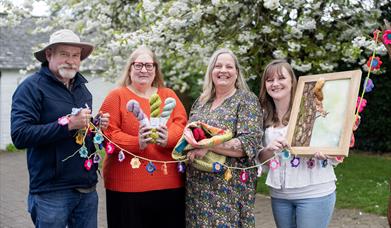 Group of festival organising team and vendor holding crocheted flower bunting and product samples in front of a flowering tree 