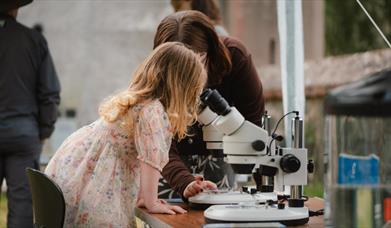 Child looking into a microscope with an adult assisting.