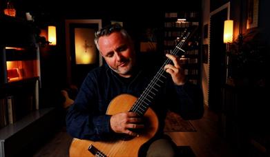 Guitarist Matthew McAllister playing guitar in a small dark room with some mood lighting.