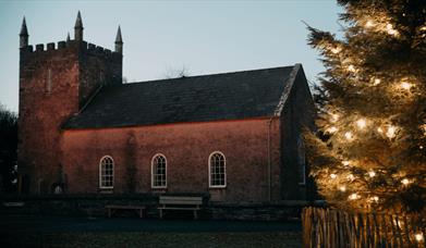 A picture of Kilmore Church at Ulster Folk Museum with a christmas tree at night