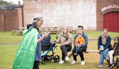 A lady dressed in a green cloak telling stories to children in the ulster folk museum
