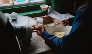 A woman scooping butter from a bowl and passing it to someone q