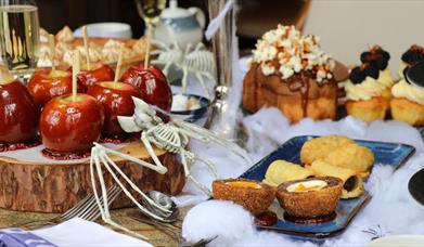 Table set up with food including toffee apples, scotch eggs, sausage rolls, cake and cupcakes with halloween decor