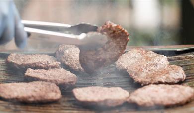 hand turning a burger on the bbq with a blue glove on it 