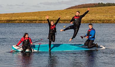 Four paddleboarders sharing a board, two of them jumping into the water