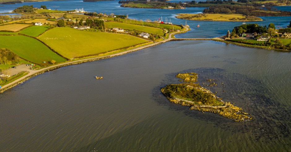 Panoramic view of the tranquil waters of Strangford Lough, a designated Area of Outstanding Natural Beauty, with small islands and distant green shorelines under a bright sky.