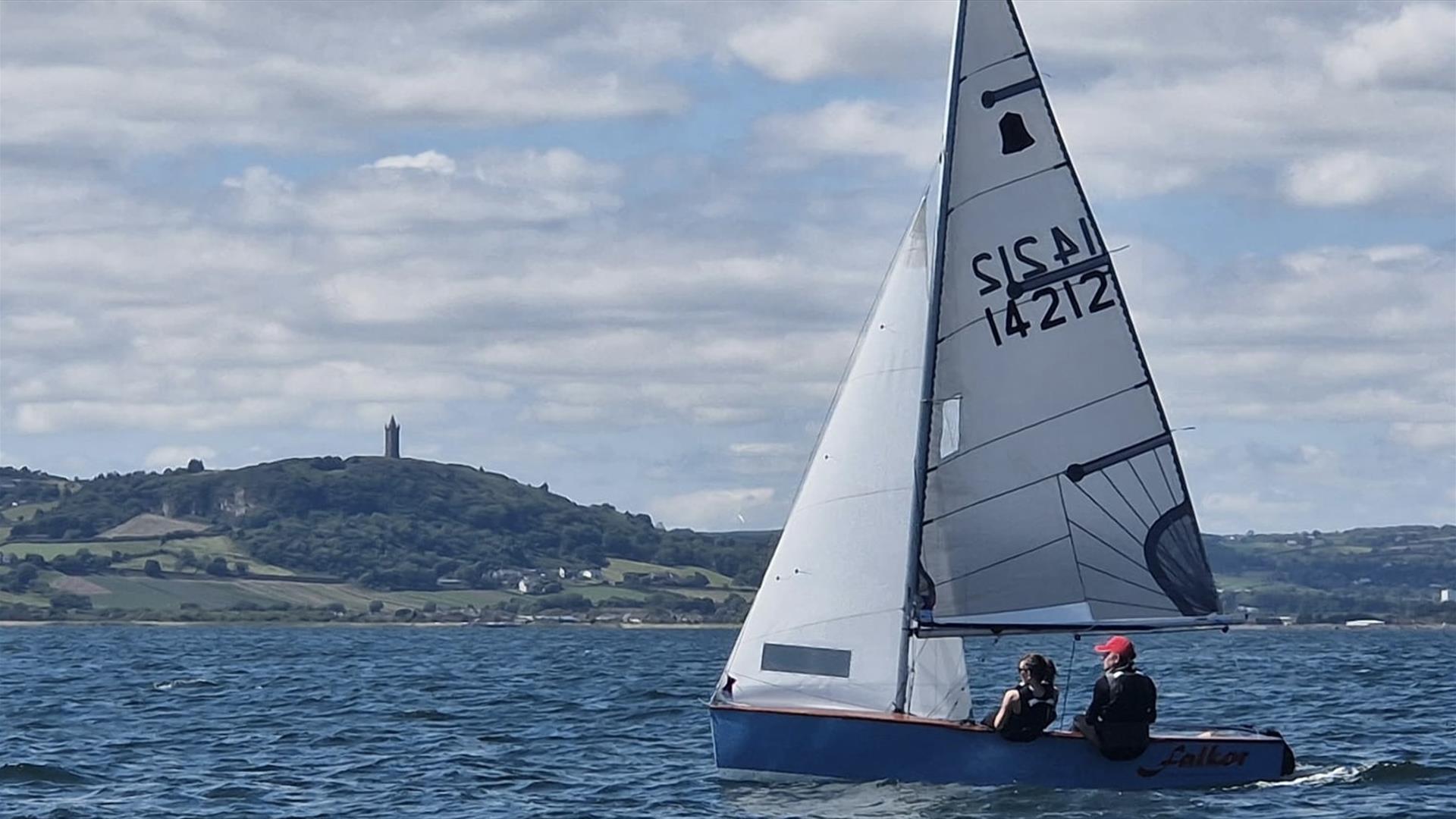 A small sailing dinghy with two people onboard, sailing on open water