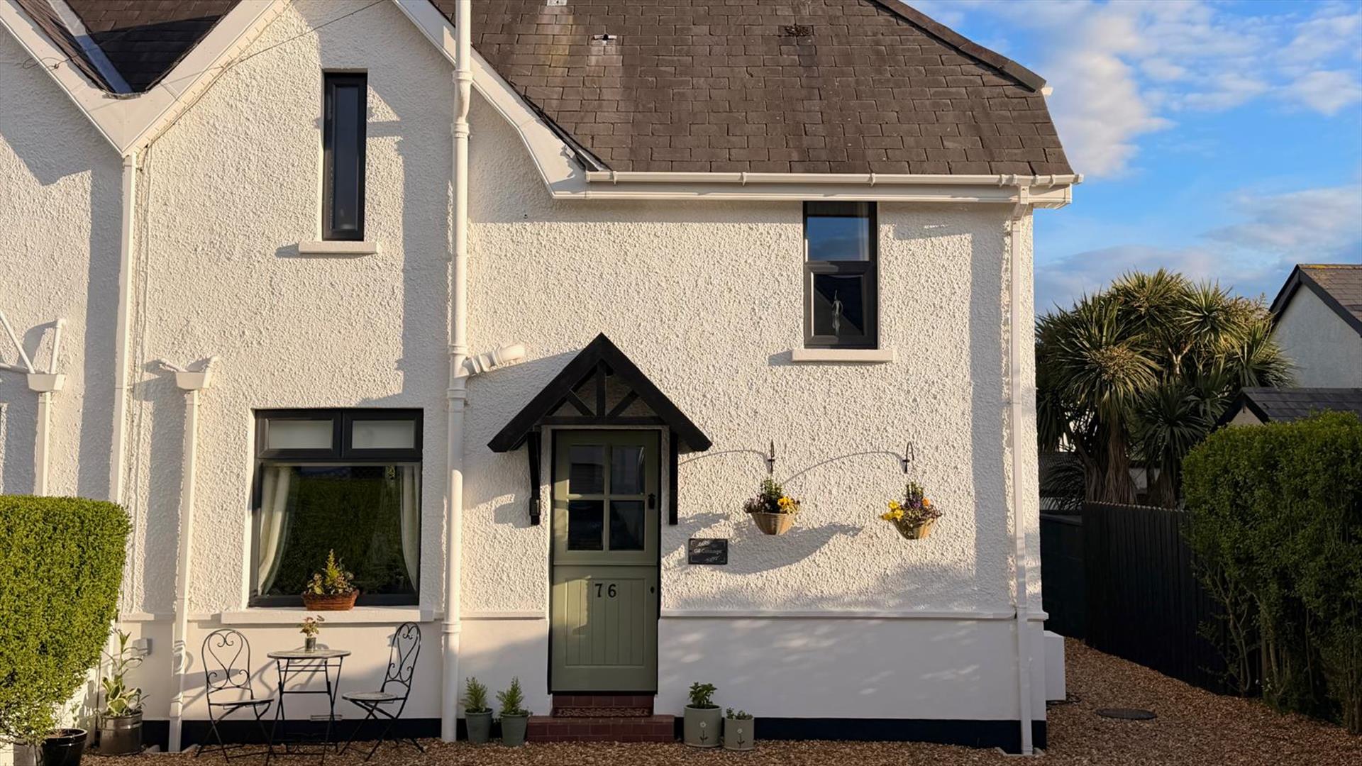 Exterior front view of Gill Cottage with a pale green front door, gravel driveway, and small outdoor seating area.