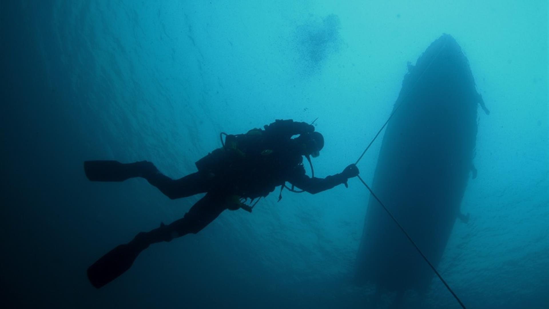 Diver underwater following an anchor line from a boat