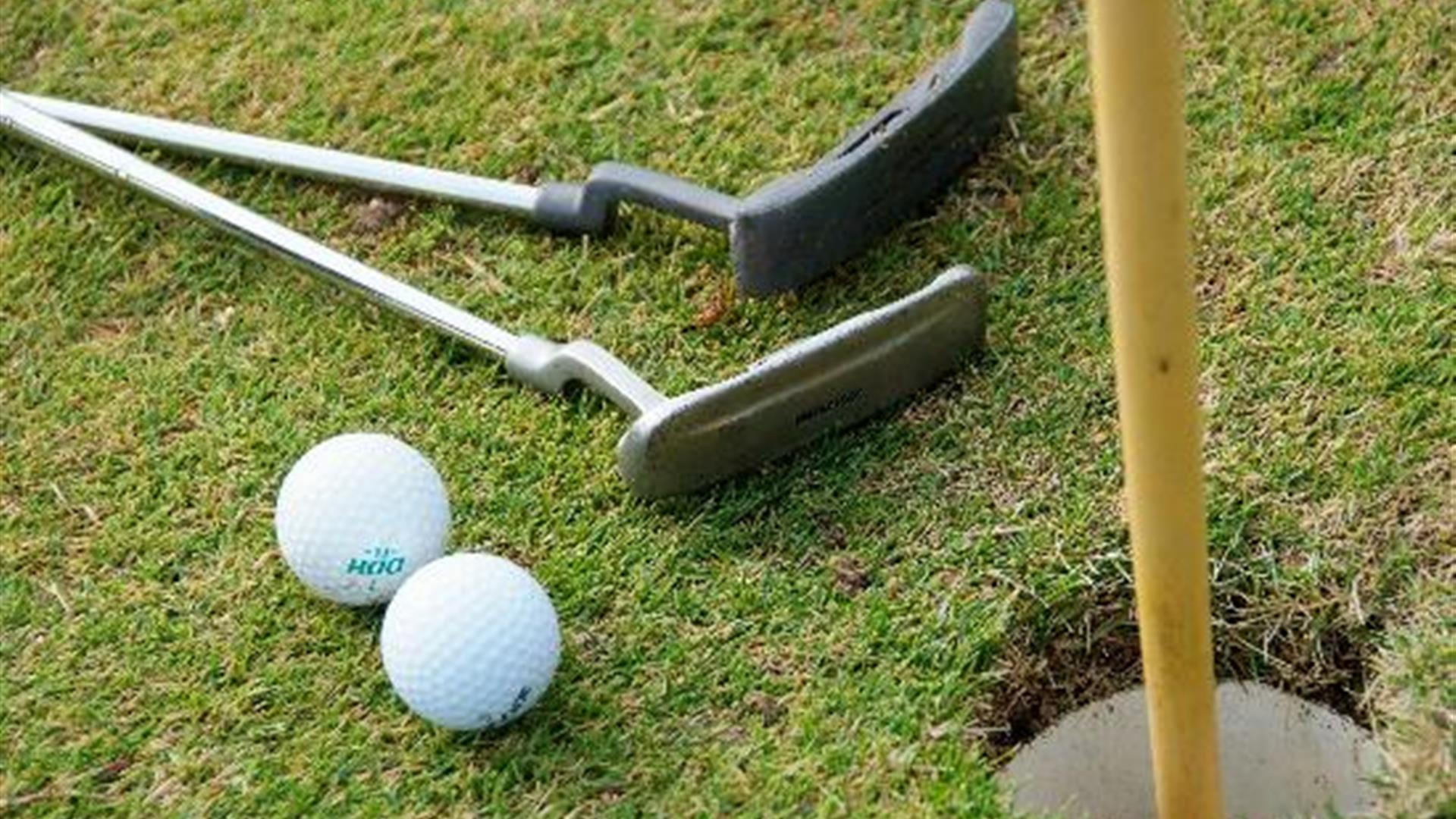 Close up photo of two putting sticks and two golf balls beside putting hole and flag at Seapark