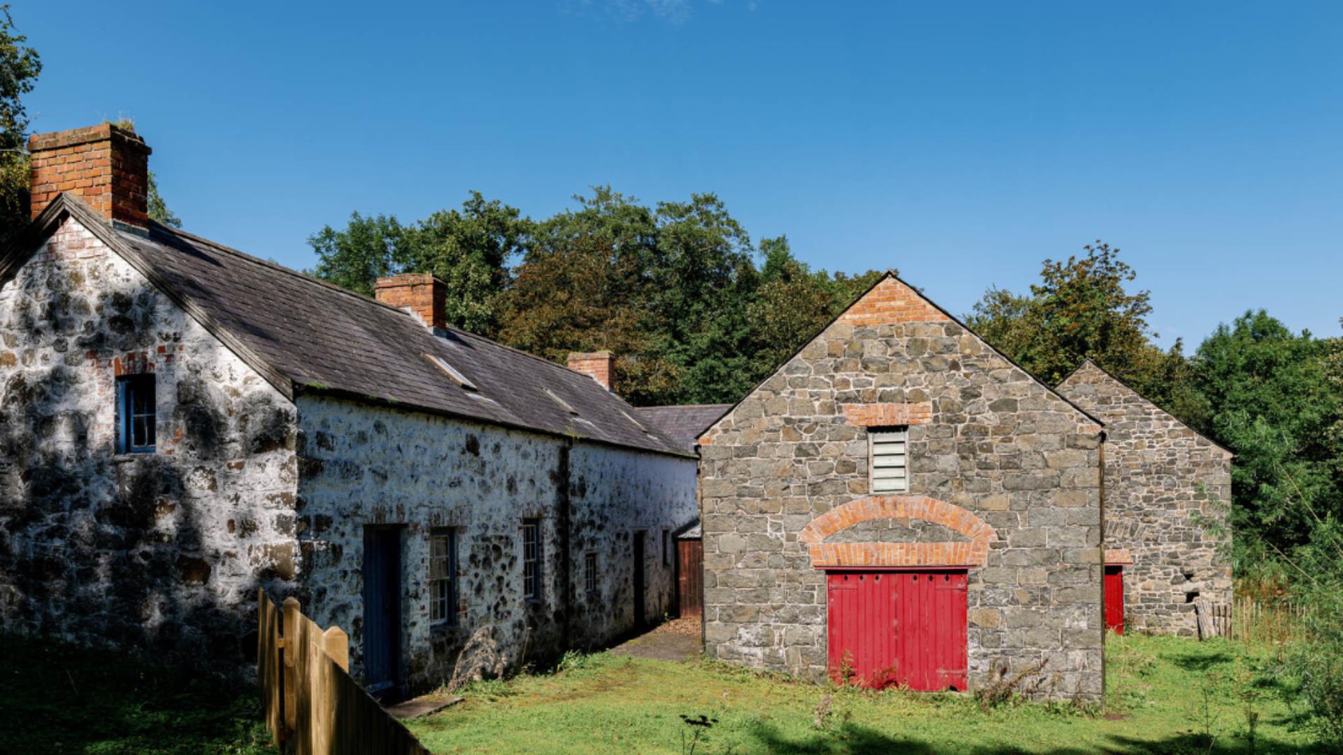Stone buildings with red doors in a grassy area under a clear sky.