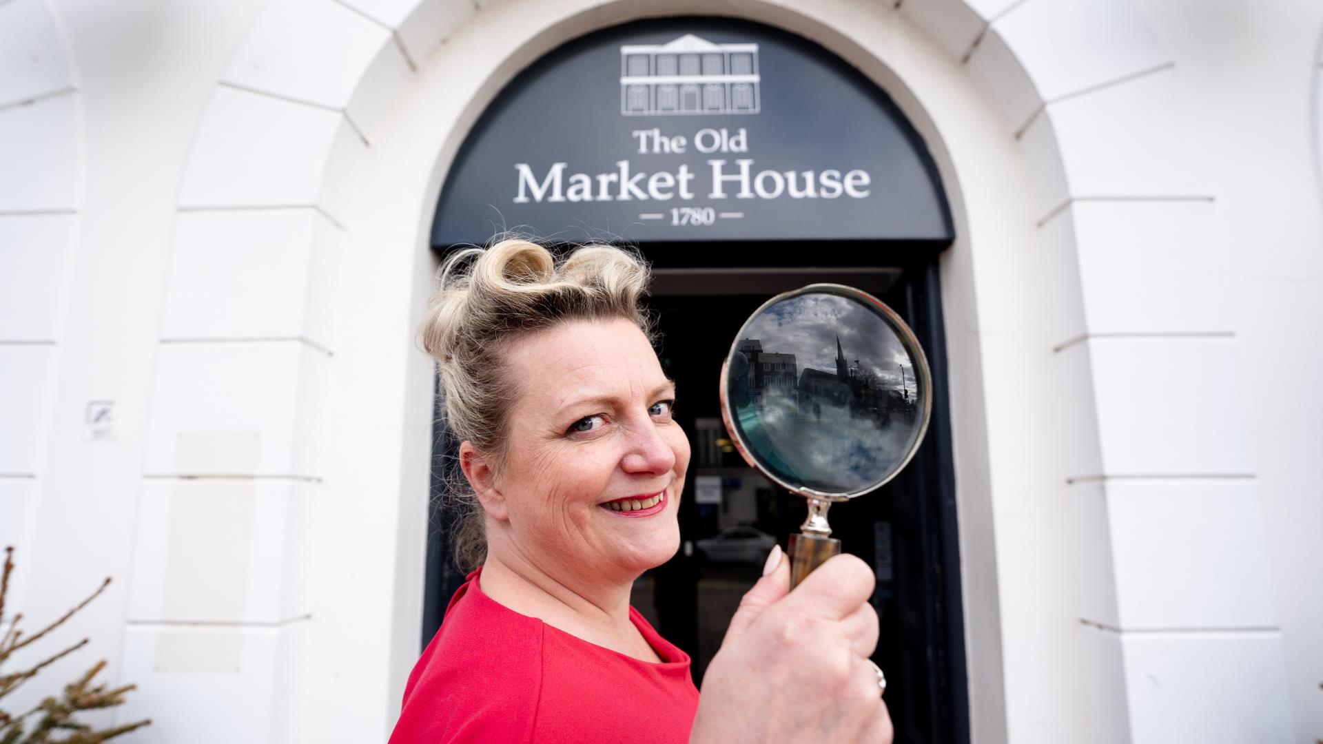 Miss Scarlett holds a magnifying glass at the doorway of The Old Market House, Bangor