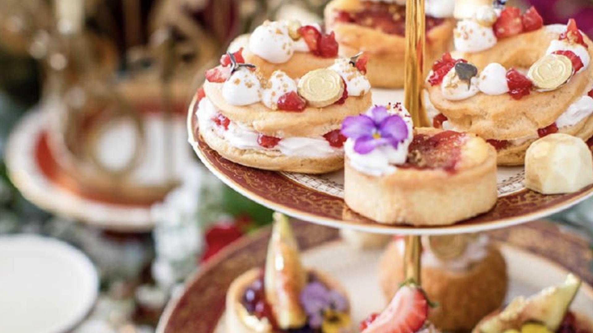 Elegant three-tiered cake stand filled with artisanal pastries, fruit tarts, and floral-decorated sweets, set against a softly blurred background with