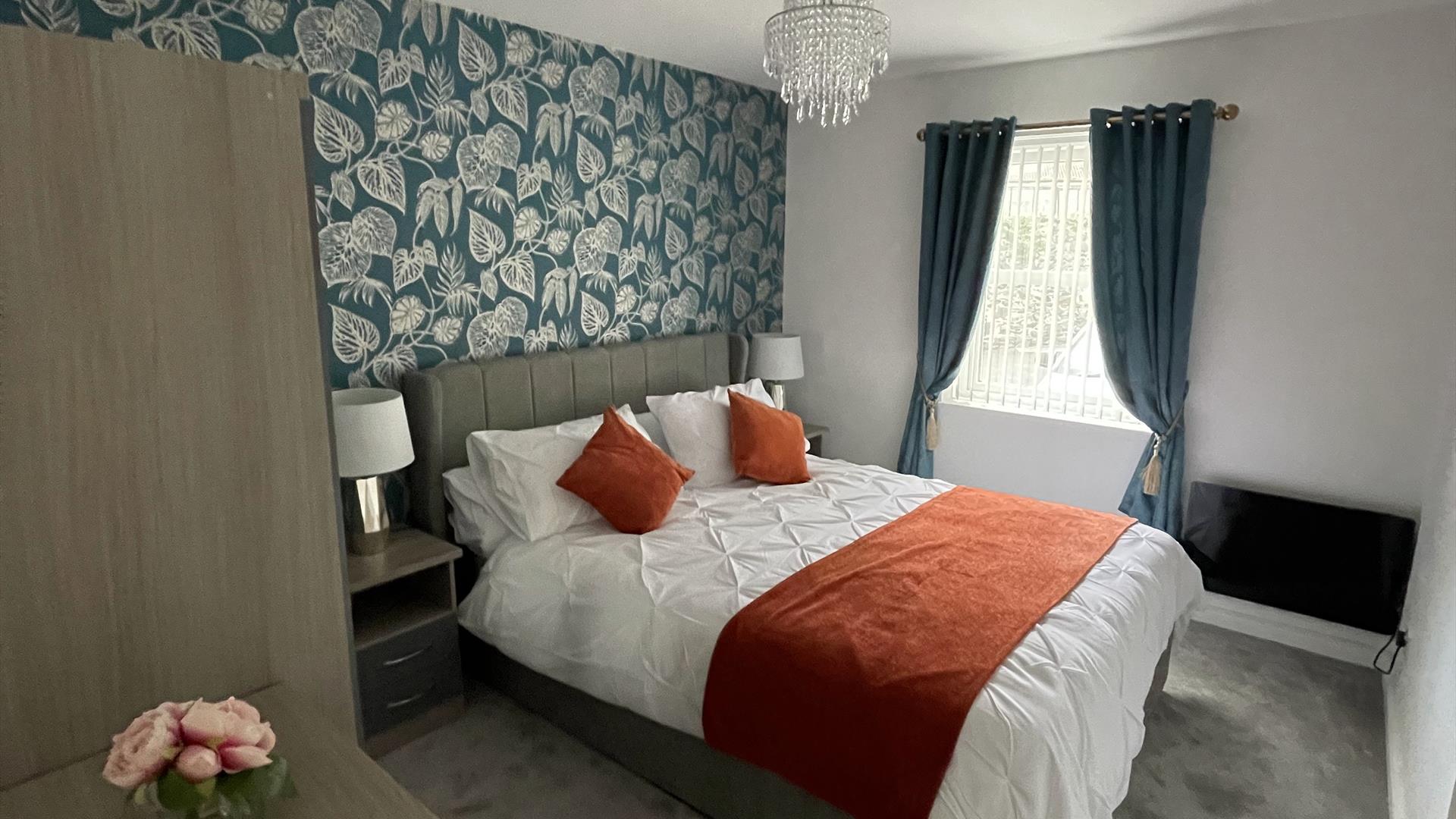 This is the master bedroom consisting of a set of drawers with a 3 door wardrobe bedisde tables in between a kingsize bed beside the window and radiat