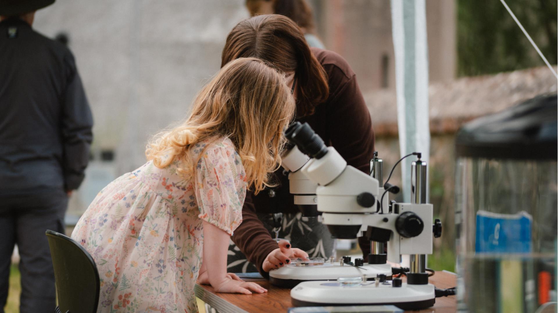 Child looking into a microscope with an adult assisting.