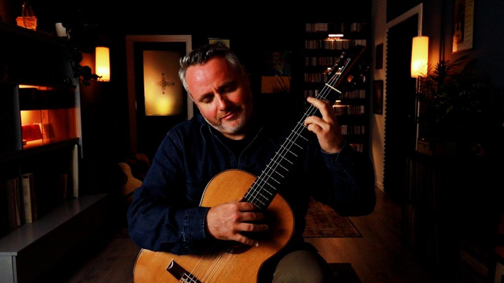 Guitarist Matthew McAllister playing guitar in a small dark room with some mood lighting.