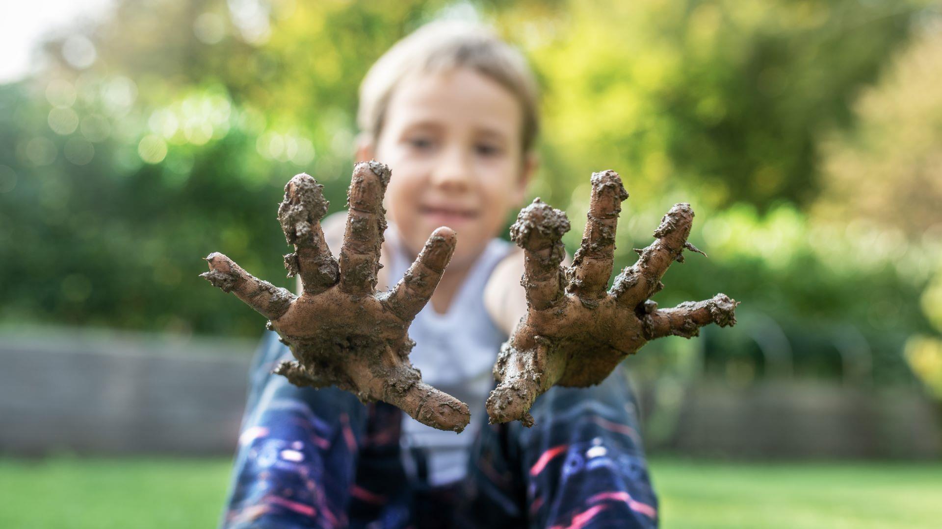 A child holding muddy hands up to the camera.