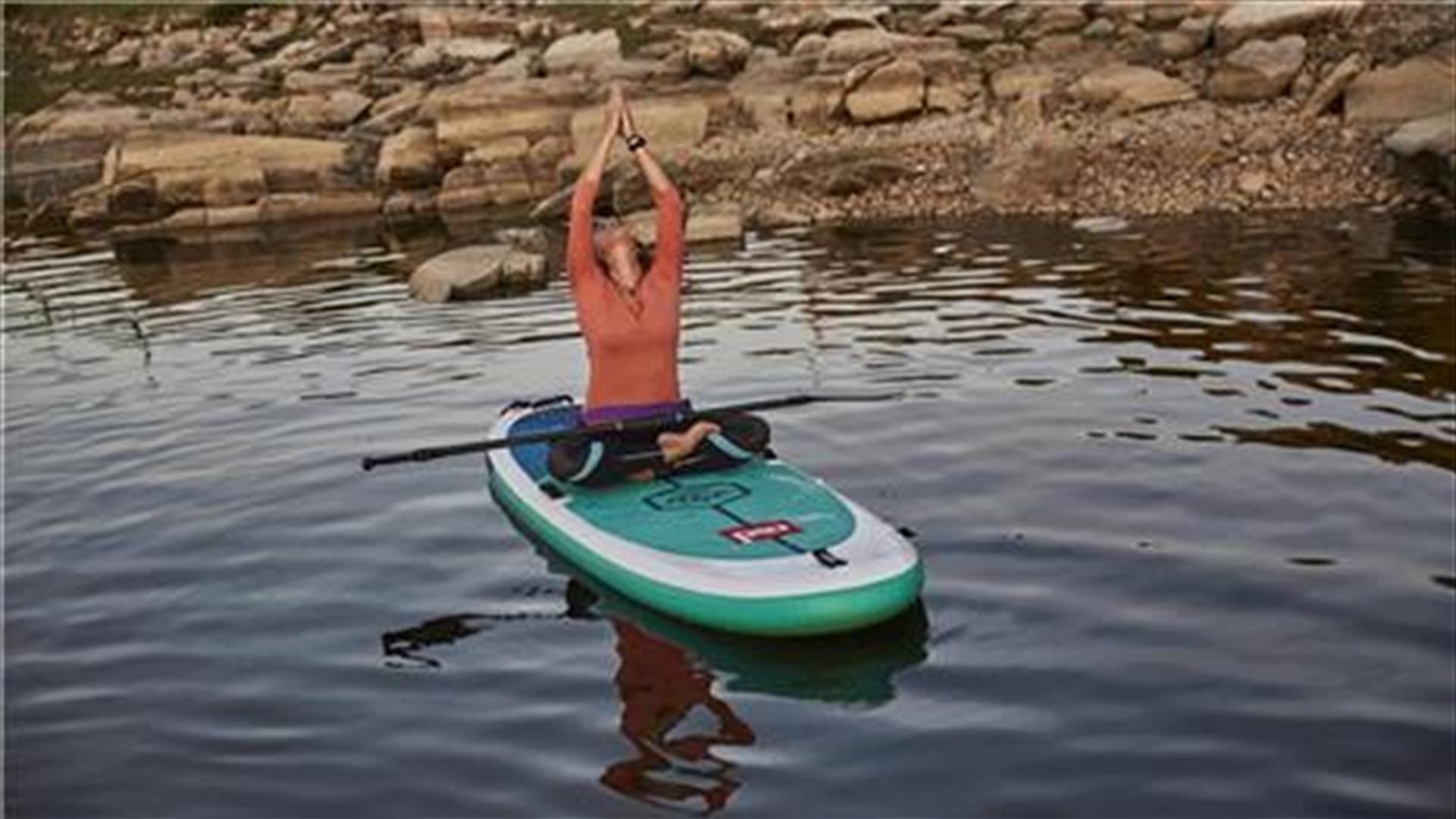 A person sitting in a yoga pose on a SUP board on water