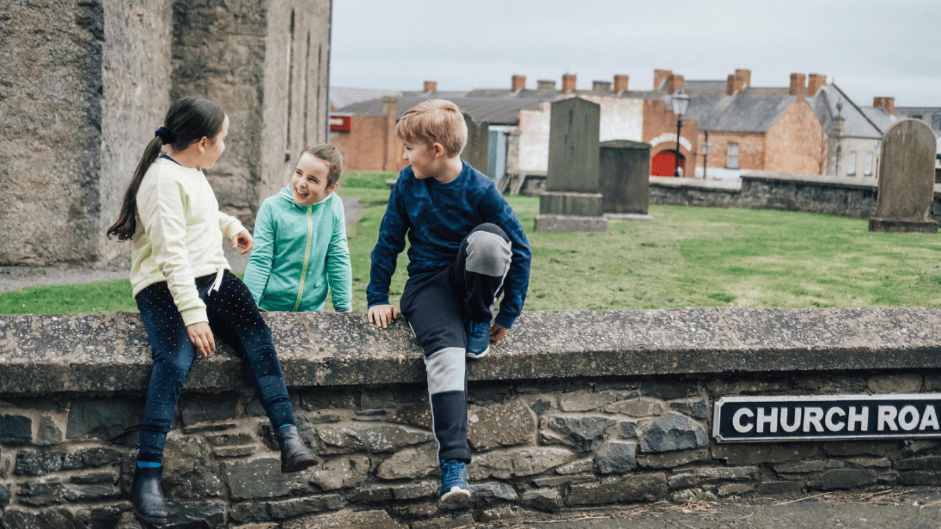 three children sitting on a stone wall at the ulster folk museum