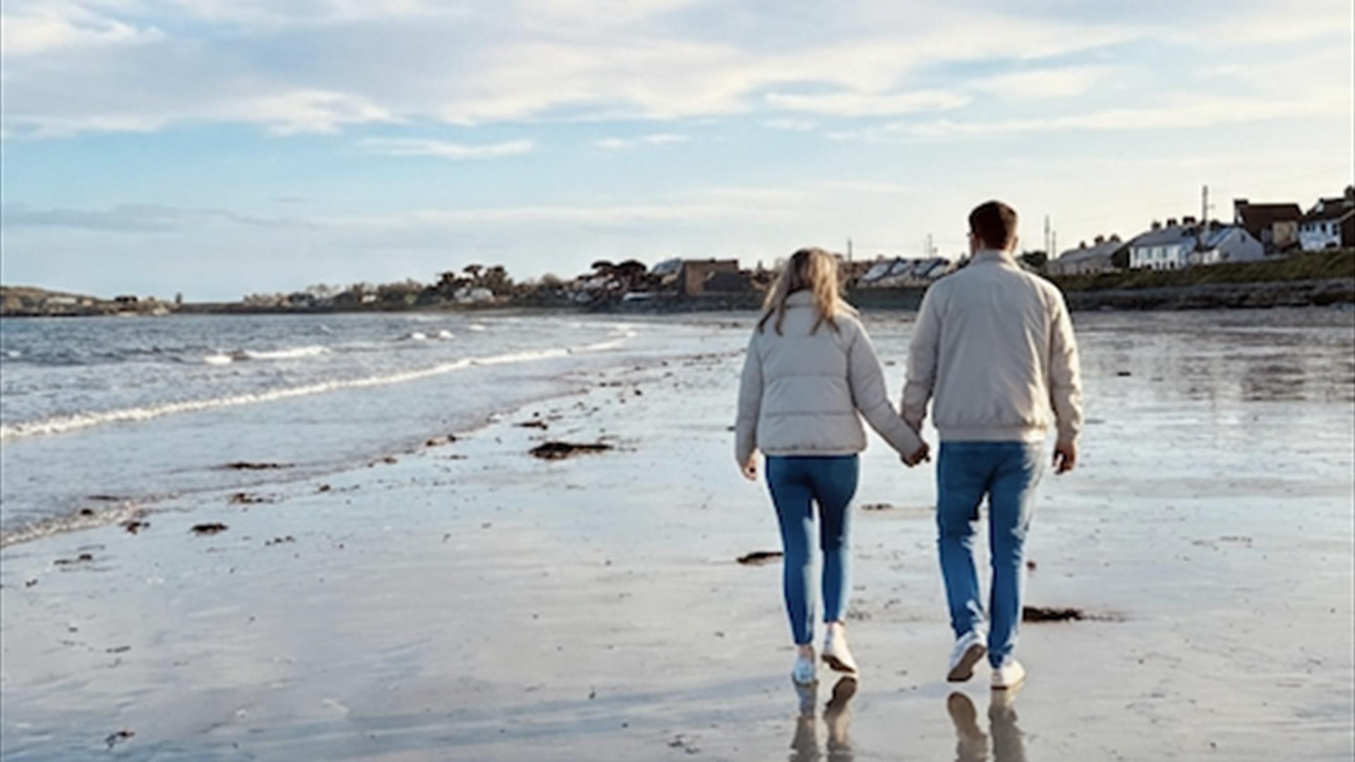 A couple walking hand in hand along Cloughey beach by the sea