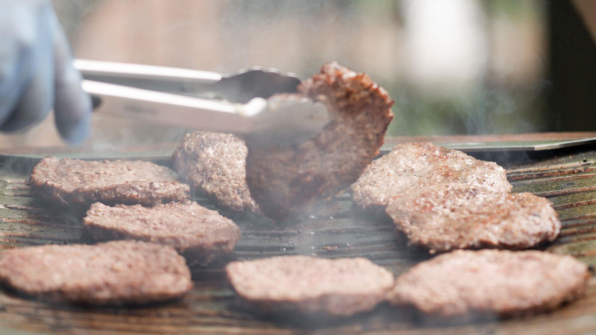 hand turning a burger on the bbq with a blue glove on it