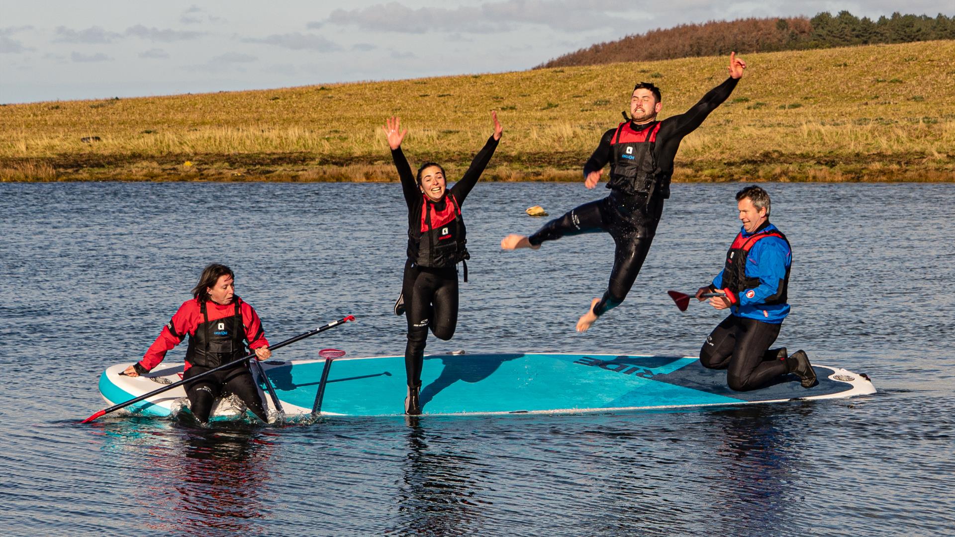 Four paddleboarders sharing a board, two of them jumping into the water