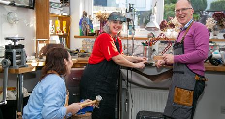 Man and Two Ladies Creating Jewellery in a Goldsmiths Workshop, Everyone is Smiling