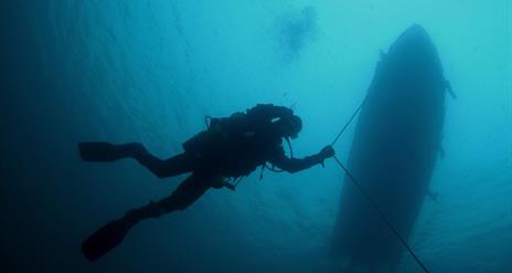 Diver underwater following an anchor line from a boat