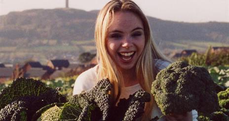 Photo of a woman holding freshly pulled vegetables with Scrabo in backdrop