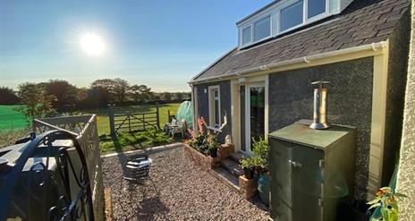 Photo of outside of the accommodation with fields, blue sky and sunshine